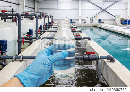 Water treatment facility with a hand holding a sample bottle for testing Water treatment facility with a hand holding a sample bottle for testing 140860733