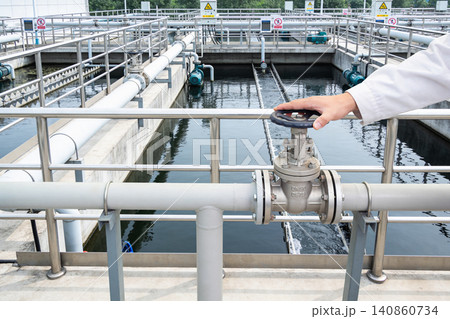 Operator adjusts valve at water treatment plant with industrial pipes and basins Operator adjusts valve at water treatment plant with industrial pipes and basins 140860734