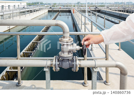 Worker operating valve at industrial water treatment plant with purification tanks Worker operating valve at industrial water treatment plant with purification tanks 140860736