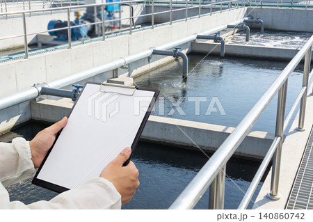 Worker in protective suit checks water treatment plant with clipboard Worker in protective suit checks water treatment plant with clipboard 140860742