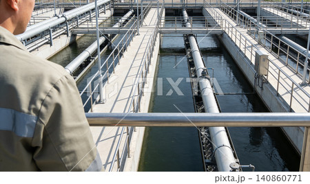 Worker observes water treatment plant with large pipes and channels Worker observes water treatment plant with large pipes and channels 140860771