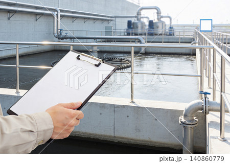 Worker inspects water treatment plant with clipboard, checking industrial processes Worker inspects water treatment plant with clipboard, checking industrial processes 140860779