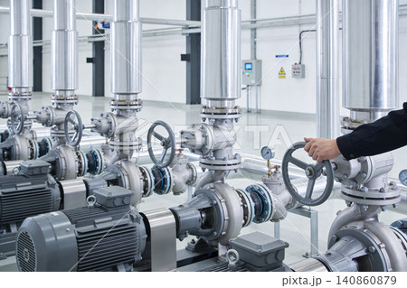 Industrial pumps and valves in a modern factory with a technician operating a control wheel Industrial pumps and valves in a modern factory with a technician operating a control wheel 140860879