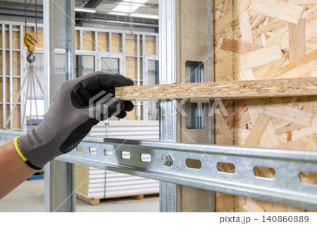 Construction worker's gloved hand places wooden board onto metal framing system Construction worker's gloved hand places wooden board onto metal framing system 140860889
