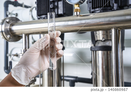 Scientist holding test tube with clear liquid near industrial water purification system Scientist holding test tube with clear liquid near industrial water purification system 140860987