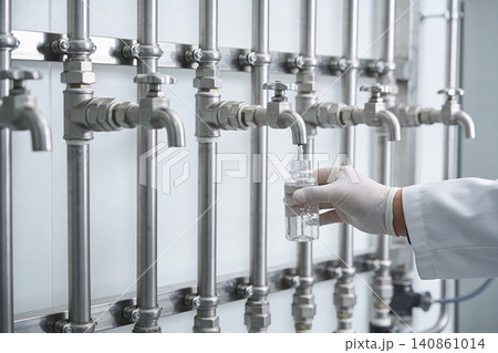 Scientist collecting liquid sample from industrial pipe system in laboratory Scientist collecting liquid sample from industrial pipe system in laboratory 140861014