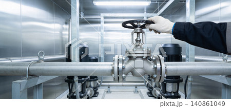 Industrial worker's gloved hand turns a large valve on a pipe system Industrial worker's gloved hand turns a large valve on a pipe system 140861049