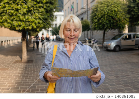 Happy senior female tourist holding paper map on beautiful European city street Happy senior female tourist holding paper map on beautiful European city street 140861085