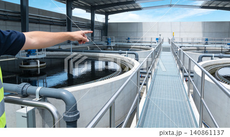 Worker points at circular clarifiers in a modern wastewater treatment plant Worker points at circular clarifiers in a modern wastewater treatment plant 140861137