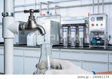 Laboratory technician collecting purified water sample from filtration system into flask Laboratory technician collecting purified water sample from filtration system into flask 140861174