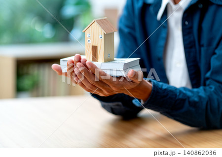 Close up man hands hold stack of money and house model in concept of collect income for home payment in the future 140862036