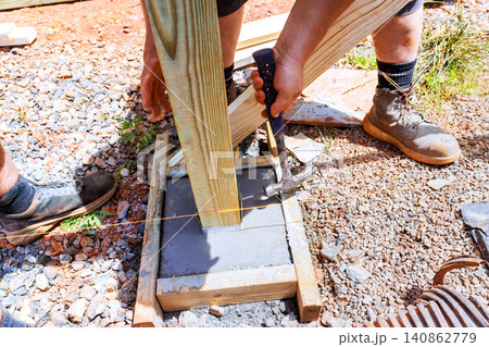 Two workers set wooden post into fresh concrete using tools on construction site Two workers set wooden post into fresh concrete using tools on construction site 140862779