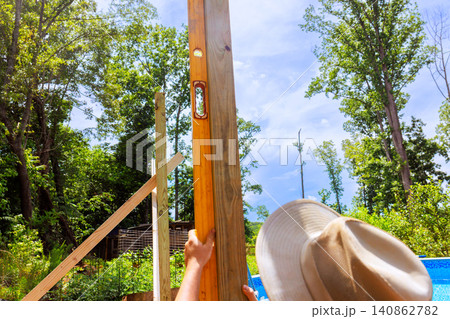Frame worker works on erecting wooden post while using level tool under construction location Frame worker works on erecting wooden post while using level tool under construction location 140862782