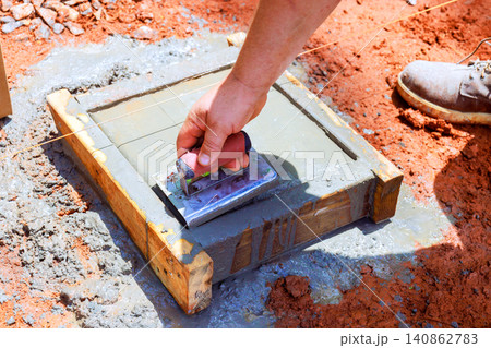 Worker uses edge trowel to smooth wet concrete in wooden frame on construction site Worker uses edge trowel to smooth wet concrete in wooden frame on construction site 140862783