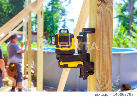 Frame workers are building structure near pool using laser level for accuracy in backyard. Frame workers are building structure near pool using laser level for accuracy in backyard. 140862798