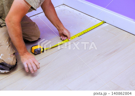 Carpenter worker uses tape measure to measure wooden floorboards in room with purple walls. Carpenter worker uses tape measure to measure wooden floorboards in room with purple walls. 140862804