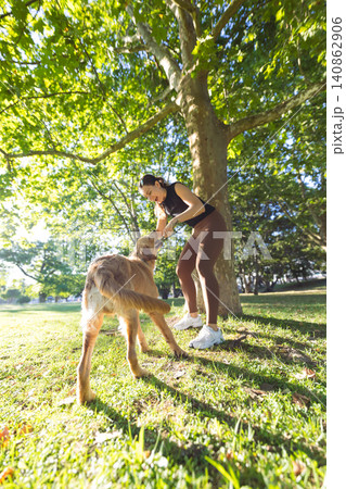 Young woman in activewear plays with a golden retriever dog in a sunny park, surrounded by green trees and grass under a clear blue sky Young woman in activewear plays with a golden retriever dog in a sunny park, surrounded by green trees and grass under a clear blue sky 140862906
