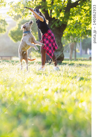 Girl plays with dog in sunny park while trees provide shade and grass is green Girl plays with dog in sunny park while trees provide shade and grass is green 140862933
