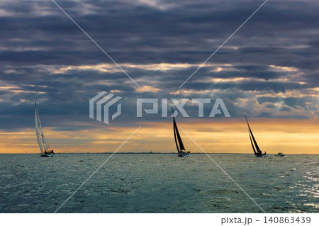 A lot of sailing boats are in sailing regatta in the Gulf of Finland at sunset, Russia, St.Petersburg, hot race of several yachts, teamwork, yachtsman A lot of sailing boats are in sailing regatta in the Gulf of Finland at sunset, Russia, St.Petersburg, hot race of several yachts, teamwork, yachtsman 140863439