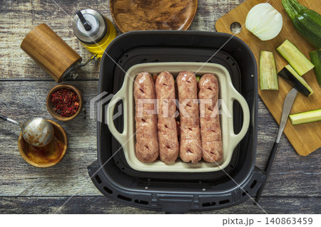 Step 7. Cooking hearty grilled sausages baked with eggplant and zucchini in an air fryer, in kitchen gadget modern. Lifestyle trendy of new cooking. Healthy cooking with air fryer. 140863459
