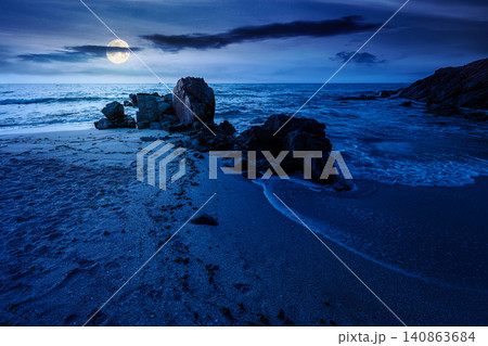 huge stones on the sandy beach at night. mysterious holiday season background at the sea. full moon over clouds on the dark sky above horizon. view of waves washing the shore huge stones on the sandy beach at night. mysterious holiday season background at the sea. full moon over clouds on the dark sky above horizon. view of waves washing the shore 140863684