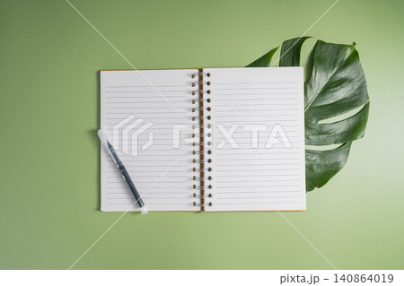 Blank open notebook with pen on green background and tropical leaf, copy space for notes 140864019