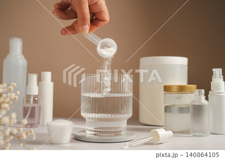 Woman adding collagen supplement to water alongside skincare products and self care routine 140864105