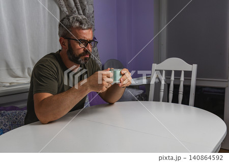Adult man enjoys coffee while sitting at home workspace during morning break Adult man enjoys coffee while sitting at home workspace during morning break 140864592