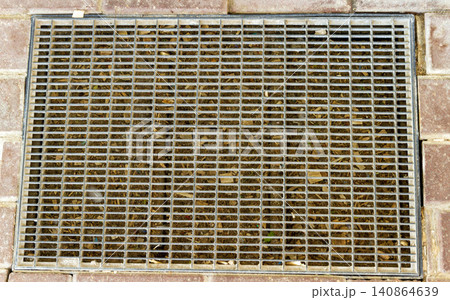 Top view of a rectangular metal drainage grate and scraper mat embedded in a brick pavement walkway. Top view of a rectangular metal drainage grate and scraper mat embedded in a brick pavement walkway. 140864639