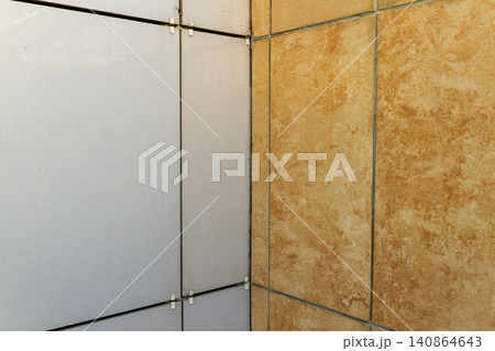 Close-up view of building facade installation showing contrasting white composite panels and orange marble texture porcelain tiles. 140864643