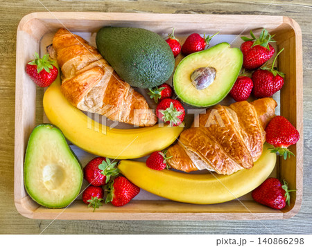 Healthy and delicious breakfast platter with fresh croissants, avocado halves, bananas and strawberries in a wooden tray. Top view. Wooden box filled with morning food. Healthy lifestyle concept. High Healthy and delicious breakfast platter with fresh croissants, avocado halves, bananas and strawberries in a wooden tray. Top view. Wooden box filled with morning food. Healthy lifestyle concept. High 140866298