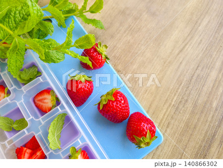 Preparing ice cubes with fresh strawberries and mint leaves in a plastic tray on a wooden table. High angle view. Summer refreshing drinks ingredients. Fresh strawberry and green mint in ice cube tray Preparing ice cubes with fresh strawberries and mint leaves in a plastic tray on a wooden table. High angle view. Summer refreshing drinks ingredients. Fresh strawberry and green mint in ice cube tray 140866302