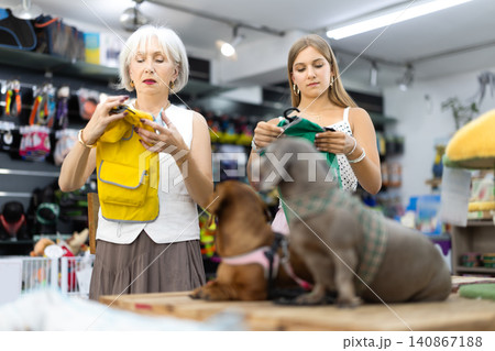 Girl and woman choosing dog coats for two dogs in pet store Girl and woman choosing dog coats for two dogs in pet store 140867188