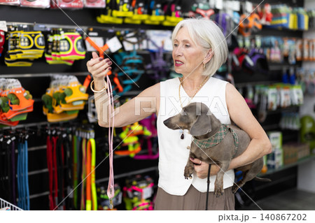 Elderly woman with dog choosing leash in pet store Elderly woman with dog choosing leash in pet store 140867202
