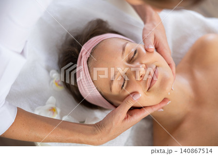 Young woman enjoying professional facial massage in beauty salon 140867514