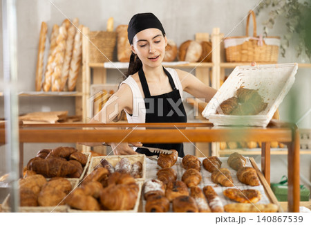 Young woman seller puts croissants in showcase 140867539