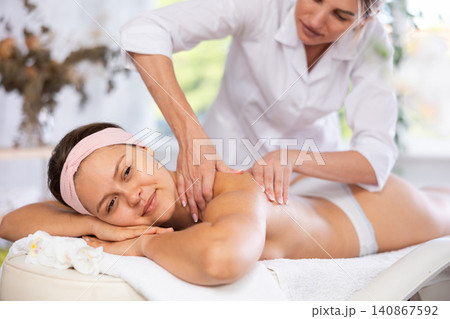 Young woman enjoying back and shoulders massage from professional masseuse Young woman enjoying back and shoulders massage from professional masseuse 140867592