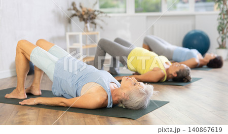 Old woman practicing bridge pose of yoga in training room during fitness classes 140867619