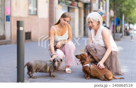 Girl and elderly woman sitting with dogs and talking outdoors 140868519