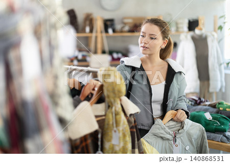 Female shopper carefully selects a fashionable jacket in clothing boutique. Female shopper carefully selects a fashionable jacket in clothing boutique. 140868531