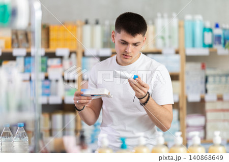 Attentive young guy buyer choosing medical ointment and reading composition of medicine on box in pharmacy Attentive young guy buyer choosing medical ointment and reading composition of medicine on box in pharmacy 140868649
