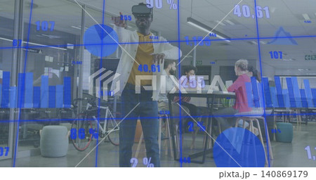 Demonstrating man wearing VR headset, cardigan and jeans gesturing at AR charts in open-plan office 140869179