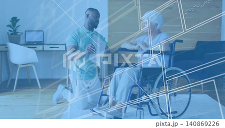 Explaining caregiver wearing polo kneeling beside senior in wheelchair at home, holding tablet HUD 140869226