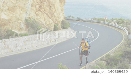 Walking hiker wearing yellow top and shorts along coastal road with backpack and poles, copy space Walking hiker wearing yellow top and shorts along coastal road with backpack and poles, copy space 140869429