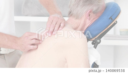 Therapist in light shirt using hands kneading shirtless client's upper-back in clinic, blue cradle Therapist in light shirt using hands kneading shirtless client's upper-back in clinic, blue cradle 140869538