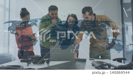 Analyzing team in orange tan attire pointing at laptop at office table, with drone, projected map 140869544