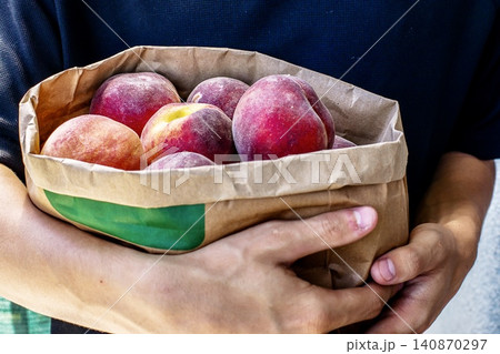 Man holding a paper bag filled with ripe fresh peaches close up 140870297