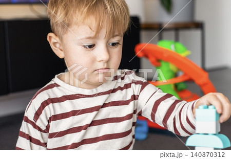 A cute little boy concentration on playing with large educational bricks, stacking a colorful toy tower on the floor in a living room. A cute little boy concentration on playing with large educational bricks, stacking a colorful toy tower on the floor in a living room. 140870312