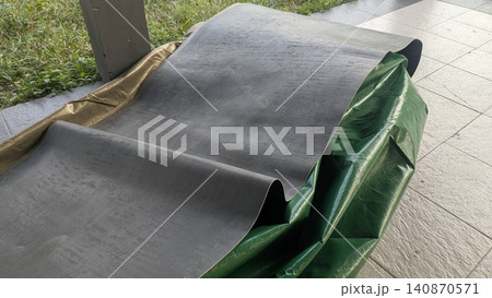 A high angle perspective captures a rolled out black textured rubber mat sheet on a grey tiled terrace floor next to a green tarp. This outdoor setup creates a simple minimalist backdrop layout A high angle perspective captures a rolled out black textured rubber mat sheet on a grey tiled terrace floor next to a green tarp. This outdoor setup creates a simple minimalist backdrop layout 140870571