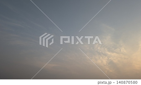 A horizontal wide angle perspective captures a calm dawn sky with subtle wispy clouds receiving soft dawn color highlights. The simple natural gradient backdrop layout template offers beautiful open 140870580